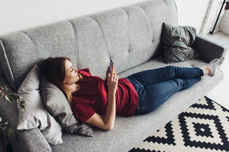 A young woman lying on a couch using a smartphone.