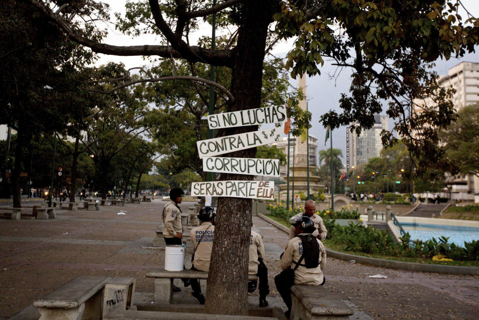 Bolivarian National Police officers sit under the shade of a tree, with placards that read in Spanish; "If you don't fight against corruption, you will be part of it," as they take a break from clashes with anti-government protesters in Caracas,Venezuela, Saturday, March 8, 2014. Venezuelans returned to the streets for the "empty pots march" to highlight growing frustration with shortages of some everyday items. Later Saturday, several hundred student protesters trying to block streets with barricades skirmished with tear gas-firing riot police in Caracas' wealthy Chacao district in what has become a nearly daily ritual. (AP Photo/Fernando Llano)