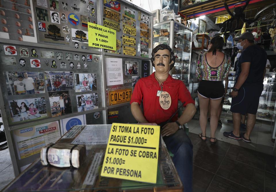 Tourists buy souvenirs of the late drug baron Pablo Escobar, featured as a statue with a sign that says one will be charged for taking photos inside a store in Doradal, Colombia, Friday, Feb. 5, 2021. Escobar and his Medellin Cartel are long dead, but one of the zoo’s prized specimens is flourishing in the tropical countryside and wetlands in and around the palace-turned-theme park — the hippopotamus.(AP Photo/Fernando Vergara)