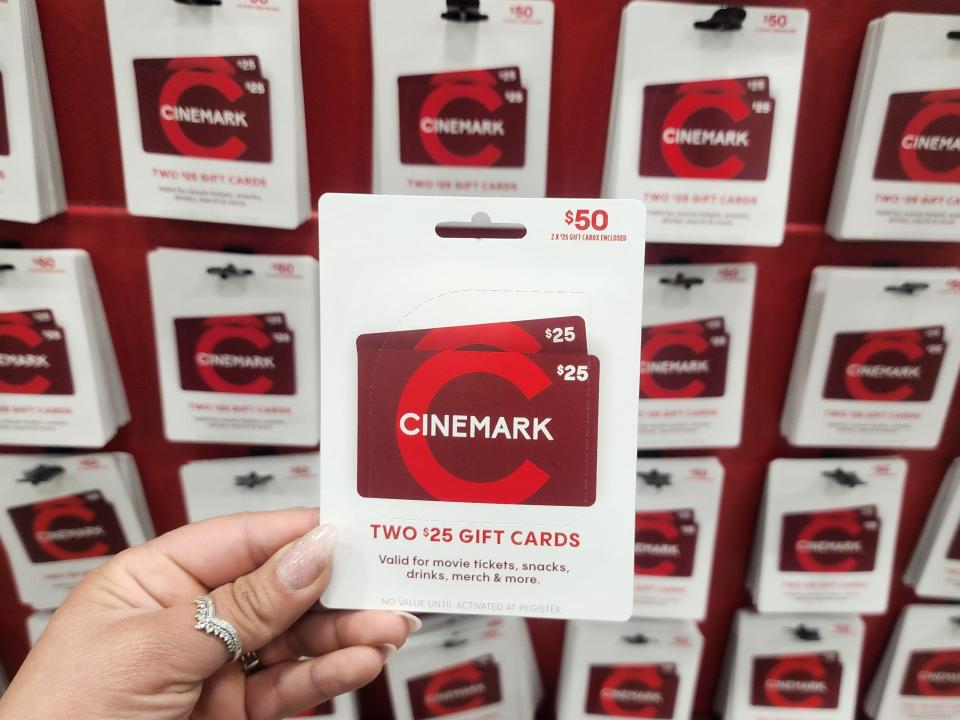A hand holding a red Cinemark gift card with a $50 value in front of a wall of Cinemark gift cards