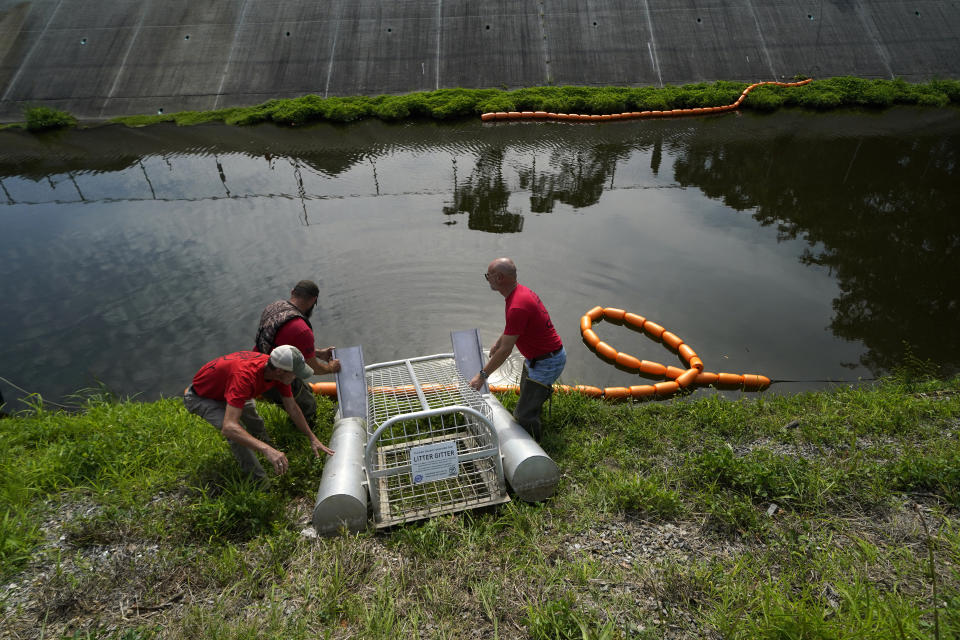 An employee of Osprey Initiative lays boom as the company installs a trap called a Litter Gitter to help collect trash floating in a canal before it can travel into larger bodies of water in Metairie, La., Thursday, May 19, 2022. Many novel devices are being used or tested worldwide to trap plastic trash in rivers and smaller streams before it can get into the ocean. (AP Photo/Gerald Herbert)