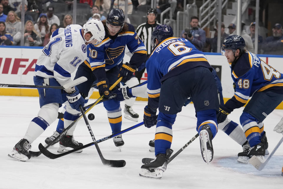 Tampa Bay Lightning's Luke Glendening (11) reaches for a loose puck as St. Louis Blues' Oskar Sundqvist (70), Marco Scandella (6) and Scott Perunovich (48) defend during the first period of an NHL hockey game Tuesday, Nov. 14, 2023, in St. Louis. (AP Photo/Jeff Roberson)