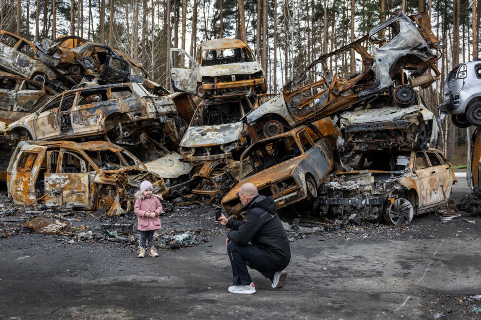 A father photographs his daughter in front of a pile of destroyed vehicles on April 21, 2022 in Irpin, Ukraine. The city was the frontline before Russian troops retreated from the area. Credit: John Moore/Getty Images