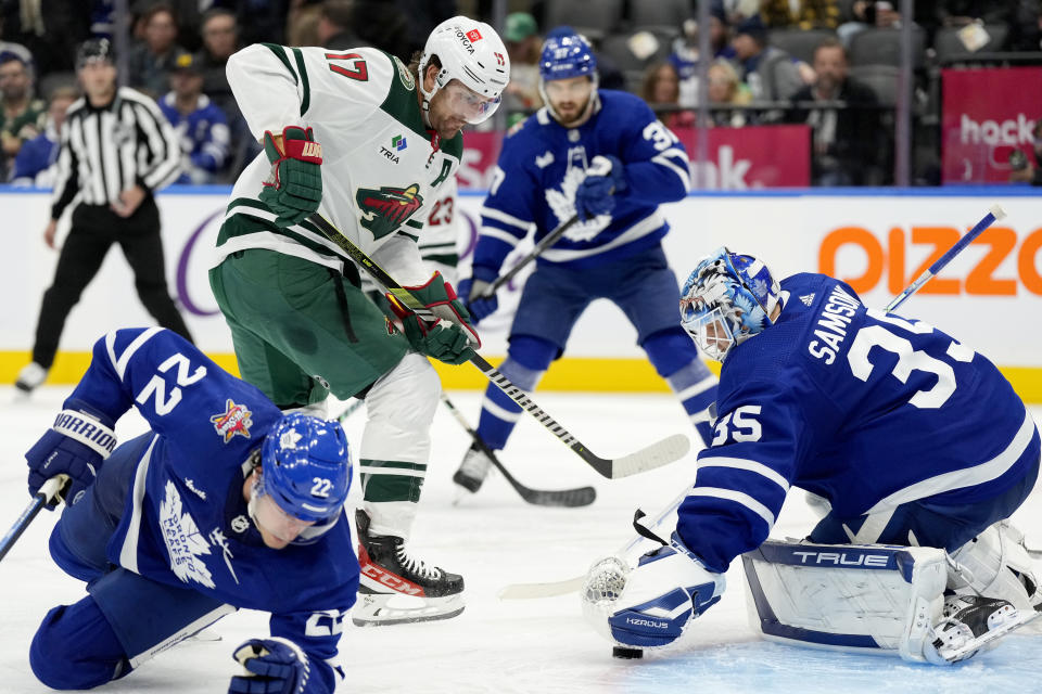 Toronto Maple Leafs goaltender Ilya Samsonov (35) makes a save against Minnesota Wild left wing Marcus Foligno (17) as Leafs' Jake McCabe (22) attempts to defend during the third period of an NHL hockey game in Toronto, Saturday, Oct. 14, 2023. (Frank Gunn/The Canadian Press via AP)