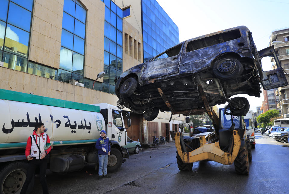 A bulldozer remove a burned mini van in front the building of Tripoli municipality that was set on fire by protesters Thursday night, during a protest against deteriorating living conditions and strict coronavirus lockdown measures, in Tripoli, Lebanon, Friday, Jan. 29, 2021. (AP Photo/Hussein Malla)