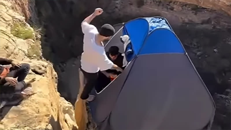  Man jumping into tent on cliff edge. 