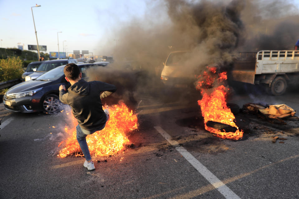 A protester kicks a burning tire that he set on fire to block a highway that links to the Beirut's international airport, during a protest against against the economic and financial crisis, in Beirut, Lebanon, Tuesday, March 2, 2021. The Lebanese pound has hit a record low against the dollar on the black market as the country's political crisis deepens and foreign currency reserves dwindle further. (AP Photo/Hussein Malla)