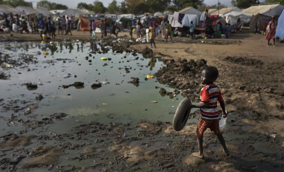 FILE - In this Sunday, Dec. 29, 2013 file photo, a displaced child holds the tyre he was using as a toy as he navigates across a muddy patch of ground to go fill an empty bottle with water from a truck, at a United Nations compound which has become home to thousands of people displaced by the recent fighting, in the capital Juba, South Sudan. The fighting in the world’s newest country has left thousands of its youngest citizens either orphans or separated from their parents, increasing their vulnerability to sickness, malnutrition and recruitment by warring groups as child soldiers. (AP Photo/Ben Curtis, File)