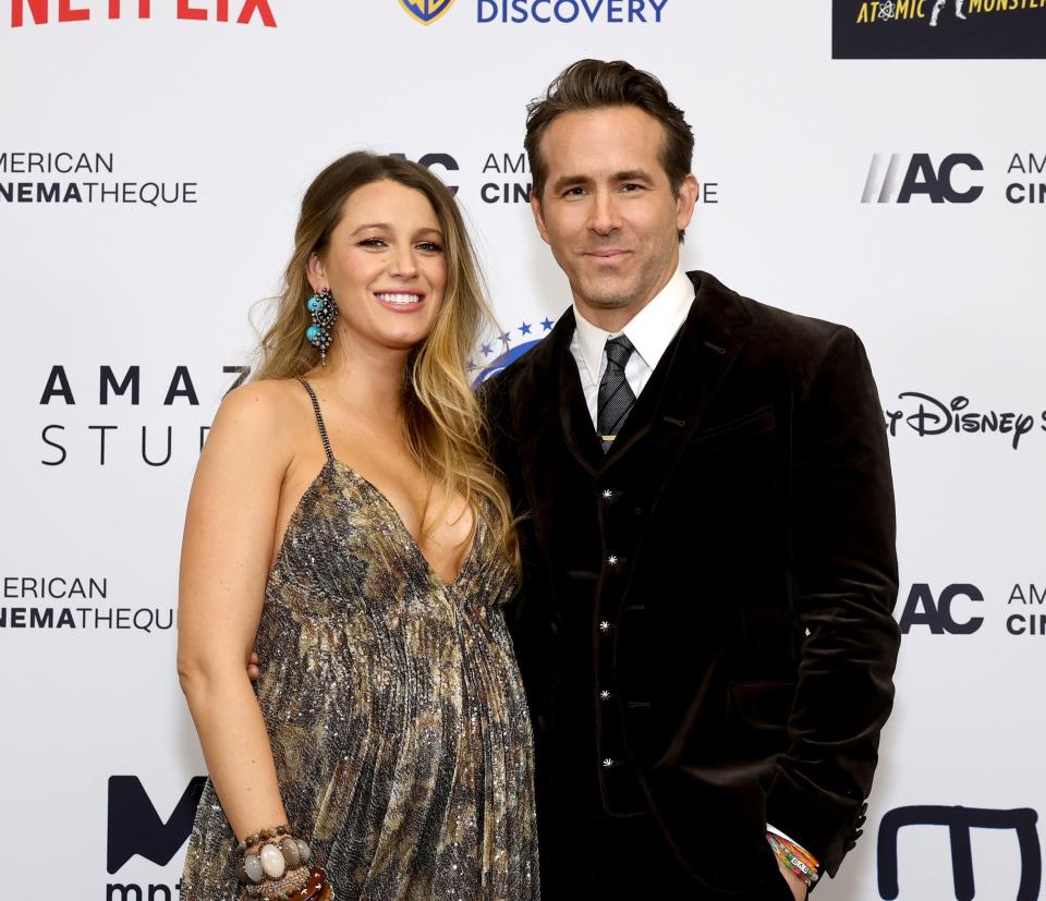 Blake Lively in a patterned dress with Ryan Reynolds in a suit, both smiling on the red carpet