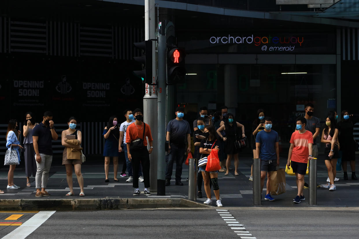 SINGAPORE - JUNE 20:  People wearing protective masks wait to cross a street at Orchard Road shopping belt on June 20, 2020 in Singapore. From June 19, Singapore started to further ease the coronavirus (COVID-19) restrictions by allowing social gatherings up to five people, re-opening of retail outlets and dining in at food and beverage outlets, subjected to safe distancing. Parks, beaches, sports amenities and public facilities in the housing estates will also reopen. However, large scale events, religious congregations, libraries, galleries and theatres will remain closed.  (Photo by Suhaimi Abdullah/Getty Images)