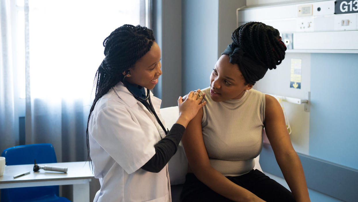 Smiling young healthcare worker talking with patient in ward.