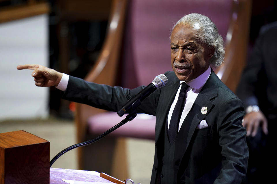 Rev. Al Sharpton, speaking at the microphone, extends his right hand to point, with a pained expression on his face. 
