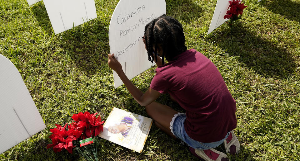 A little girl kneels at her grandmother's grave.