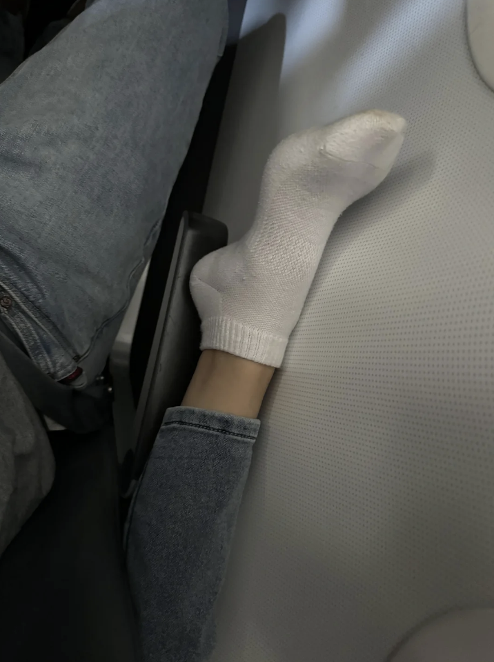 Person's sock-covered foot wedged between airplane seats, humorously appearing hand-like