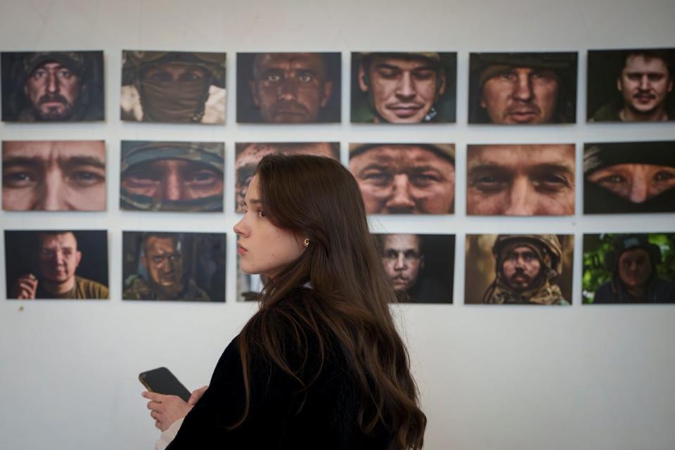 A woman pauses in front of portraits of Ukrainian servicemen displayed in a war photography exhibition by Ukrainian photographers Vlada and Kostiantyn Liberov, in Kyiv, Ukraine, Thursday, April 4, 2024.