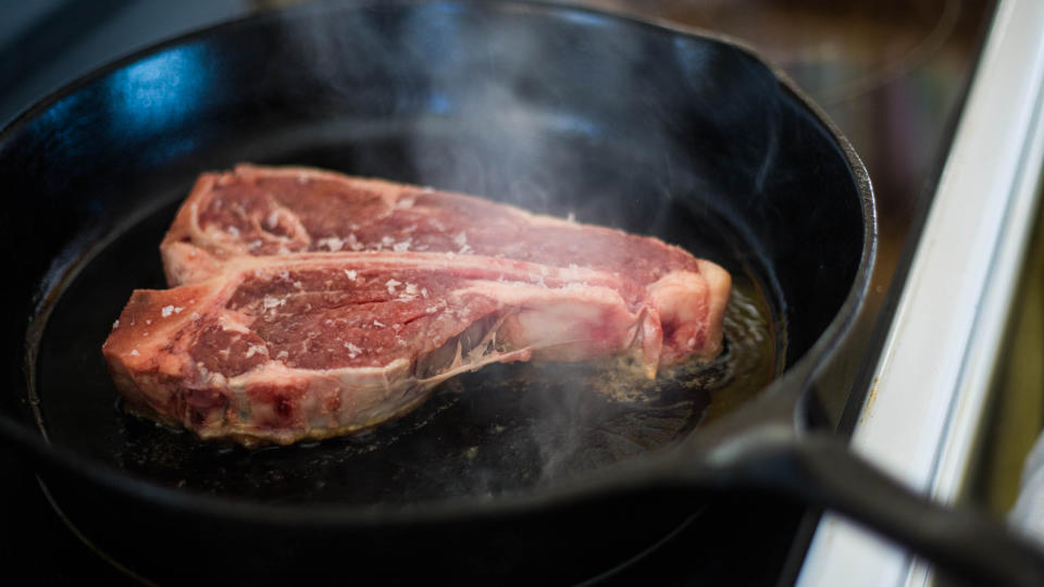 Raw steak being sprinkled with salt  being cooked in a cast iron skillet