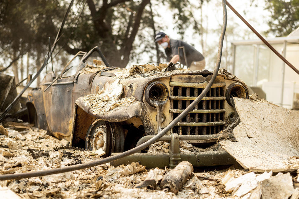 Mark Hanson goes through the remains of a 1951 Willys-Overland Jeepster following the LNU Lightning Complex fires in Vacaville, Calif., on Friday, Aug. 21, 2020. The blaze destroyed his family home as well as the Jeepster which his father purchased new and Mark rebuilt while in high school. (AP Photo/Noah Berger)