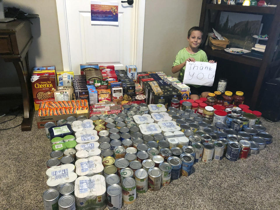 Dylan Pfeifer sits with all the donations he received during his first food drive at his home in Chandler, Ariz., in October 2020. Pfeifer received 316 cans and boxes of food. Each drive is the culmination of hours of work that involves drawing posters, going door-to-door to hand out flyers and working with his mother to post information on Facebook. (Erin Pfeifer via AP)