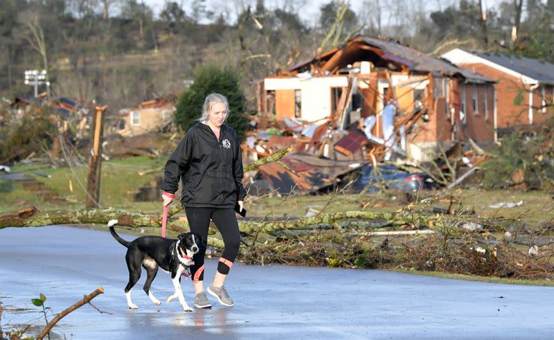 A woman walks her dog past a damaged house in Stanford Estates after a tornado touched down in Nashville