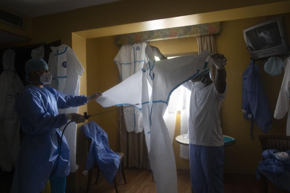 Doctors disinfect a protective suit after checking on asymptomatic COVID-19 patients quarantining at a hotel, as they remove their gear in Caracas, Venezuela, Friday, July 24, 2020. The government is offering residents this eight-floor hotel, among other hotels, to quarantine if they are asymptomatic with COVID-19, where doctors check on them and they are fed three free meals every day. (AP Photo/Ariana Cubillos)