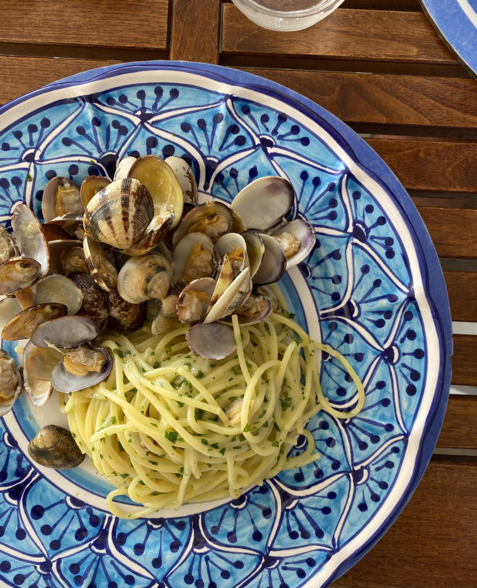 A plate of spaghetti with clams on a patterned plate, placed on a wooden table