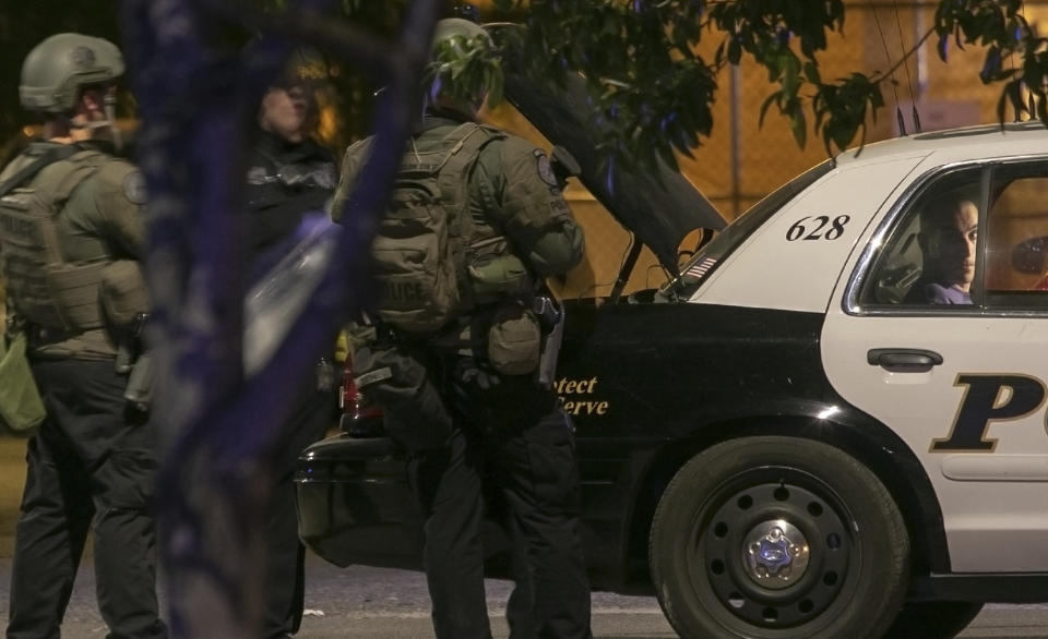 In this Thursday, Nov. 29, 2018 photo, Tucson Police Officers stand by a police car with a man detained in the back seat following a shooting in Tucson, Ariz. A deputy U.S. marshal serving a felony arrest warrant was shot and killed outside the Tucson house. (Ron Medvescek/Arizona Daily Star via AP)