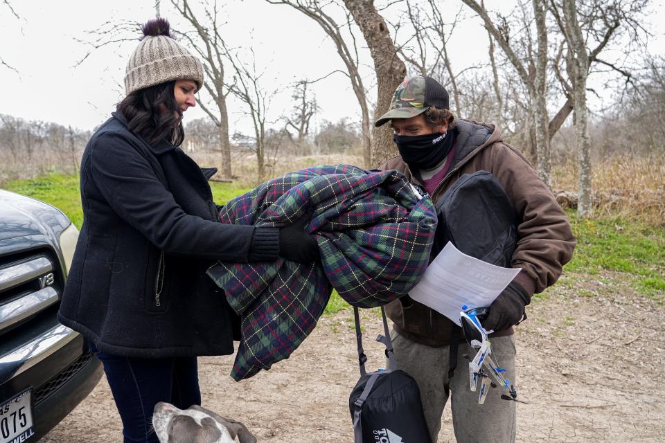 Tara McLeod, a volunteer at the Sunrise Homeless Navigation Center, gives Jack Smith a heavy blanket at a camp in South Austin on Sunday.