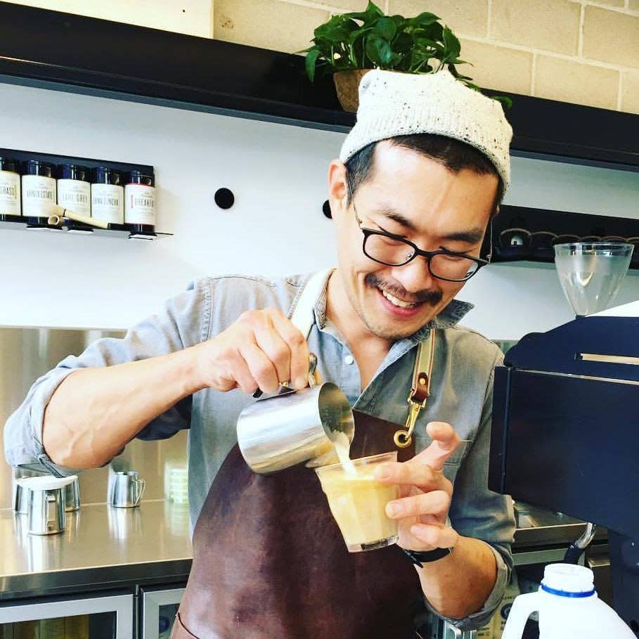 Yun-Seob Shin pours milk into a coffee while working in a cafe. 