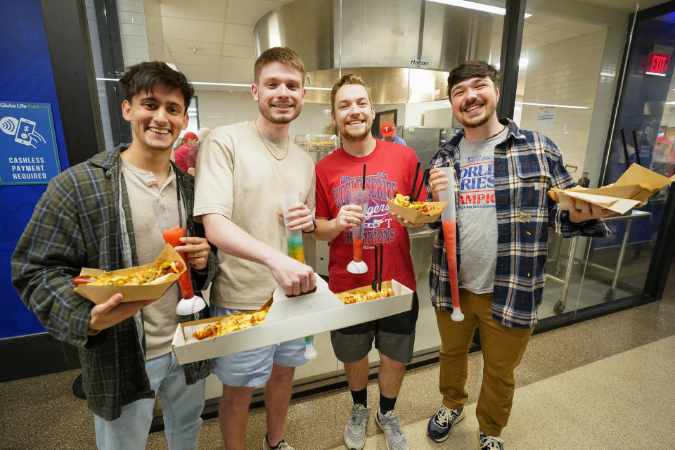 Fans hold food items, including a Broomstick hot dog, on the main concourse at Globe Life Field in Arlington, Texas, before a spring training baseball game between the Texas Rangers and the Boston Red Sox, Monday, March 25, 2024. Danielle LaFata’s been around major sports ballparks and arenas for most of her adult life, so the nutritionist has one word of advice for those who want to eat healthy when attending a Major League Baseball game this summer. Don’t. (AP Photo/Sam Hodde)