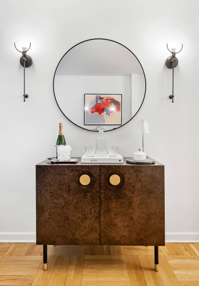 Wood bar cabinet with gold round pulls and circle mirror on wall