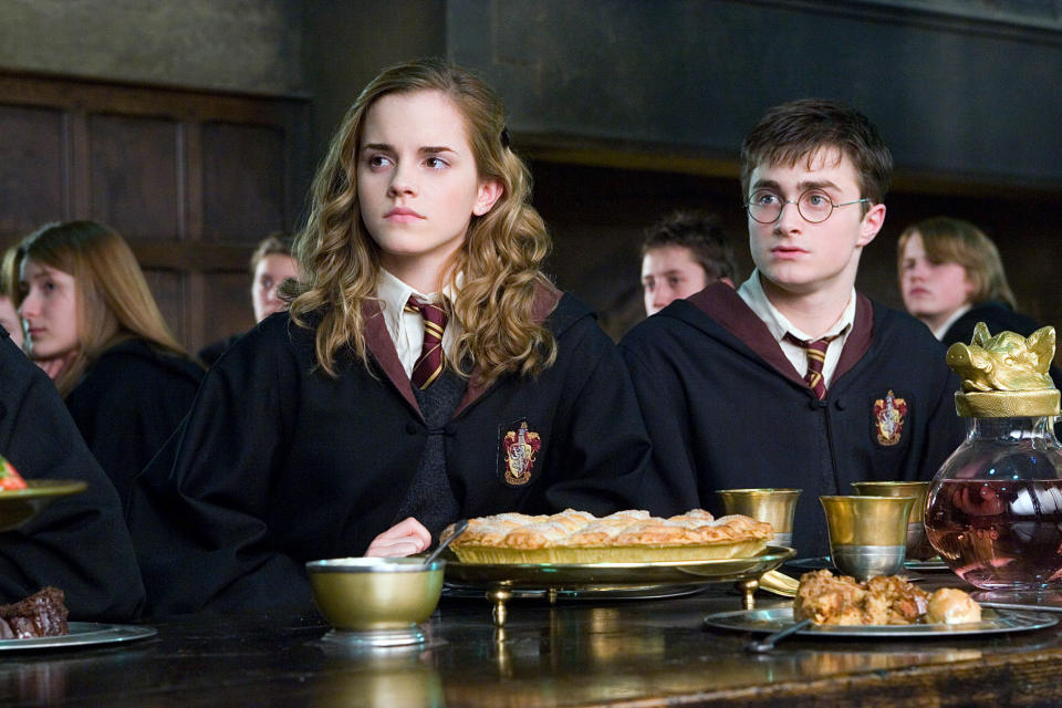Hermione and Harry from "Harry Potter" in school robes sitting at the Hogwarts dining hall