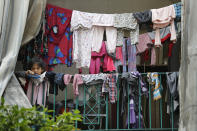 In this Saturday, May 23, 2020 photo, a Syrian girl holds her mask as she looks from her family's apartment balcony in a building where dozens of foreign workers living in overcrowded apartments have tested positive with the coronavirus, in Beirut, Lebanon. Some 250,000 registered migrant laborers in Lebanon — maids, garbage collectors, farm hands and construction workers — are growing more desperate as a crippling economic and financial crisis sets in, coupled with coronavirus restrictions. With no functioning airports and exorbitant costs of repatriation flights, many are trapped, unable to go home. (AP Photo/Hussein Malla)