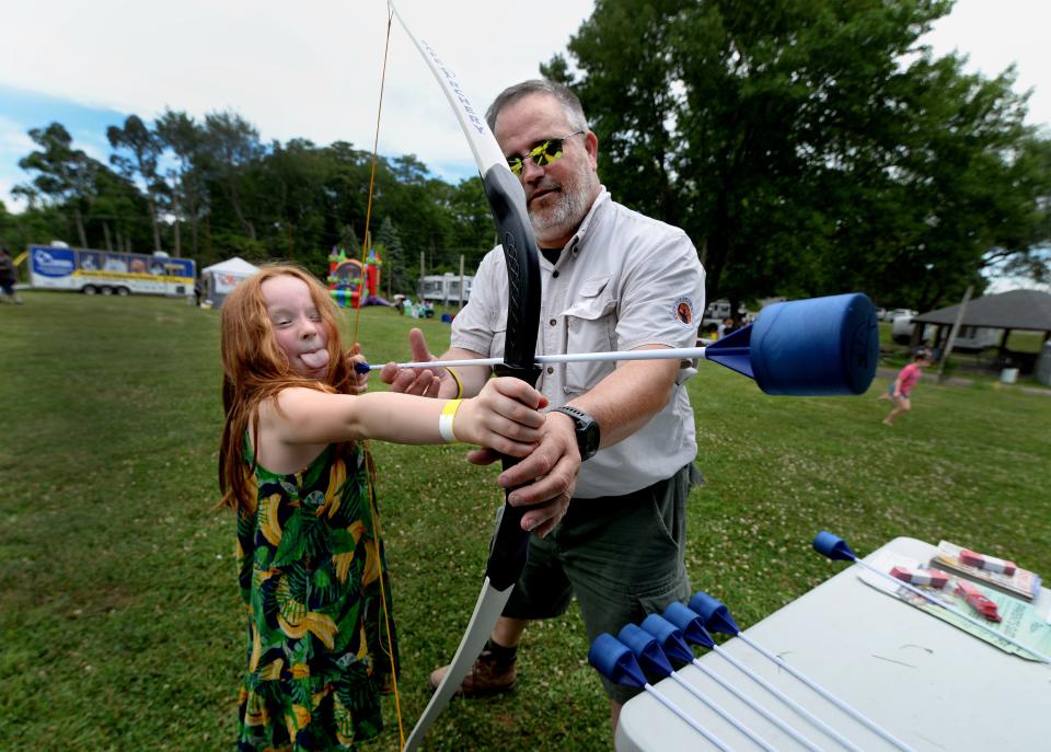 Ariel Hughes, 7, of Chatham gets some help from Jerry Daniels of the Boy Scouts as she takes aim at an inflated archery range at Dogs at the Dock event Saturday at the Lake Springfield Prop Club.