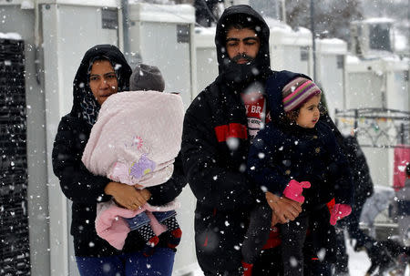 Stranded Syrian refugees carry their children through a snow storm at a refugee camp north of Athens, Greece January 10, 2017.REUTERS/Yannis Behrakis