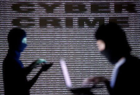 People wearing balaclavas are silhouetted as they pose with a laptops in front of a screen projected with the word 'cyber crime' and binary code, in this picture illustration taken in Zenica October 29, 2014. REUTERS/Dado Ruvic