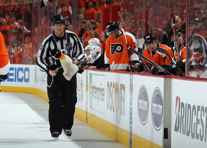 Le juge de ligne Scott Driscoll ramasse un pingouin en peluche qui a été lancé sur la patinoire pendant le 3e match de la série entre les Penguins et les Flyers, dimanche. (Photo de Bruce Bennett/Getty Images)