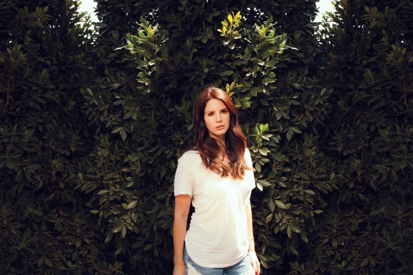 Lana Del Rey poses in front of a green, leafy area.