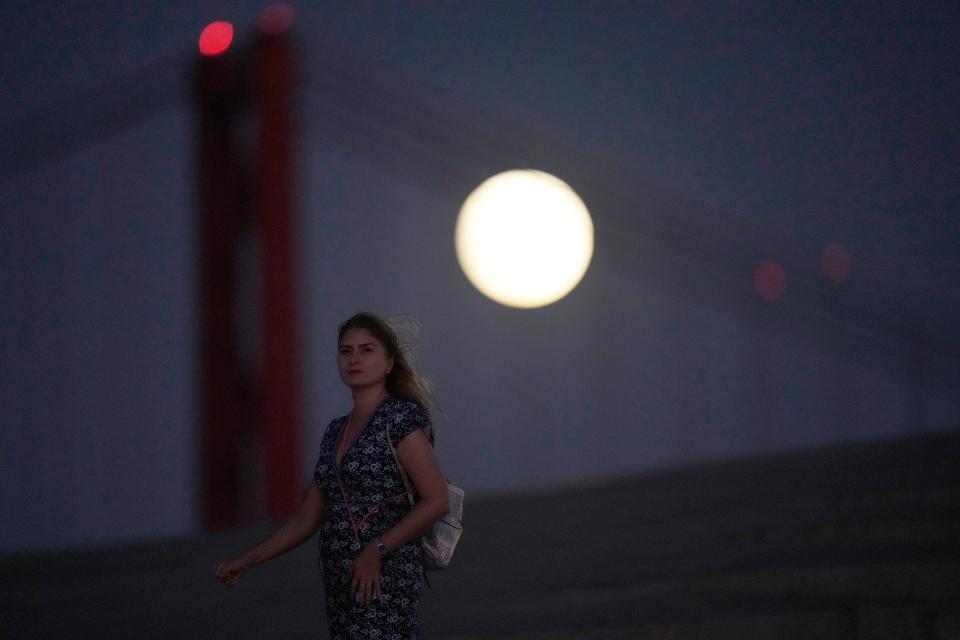 A woman walks on the roof of the Museum of Art, Architecture and Technology in Lisbon, as a full supermoon rises in the background, Thursday, Sept. 28, 2023.