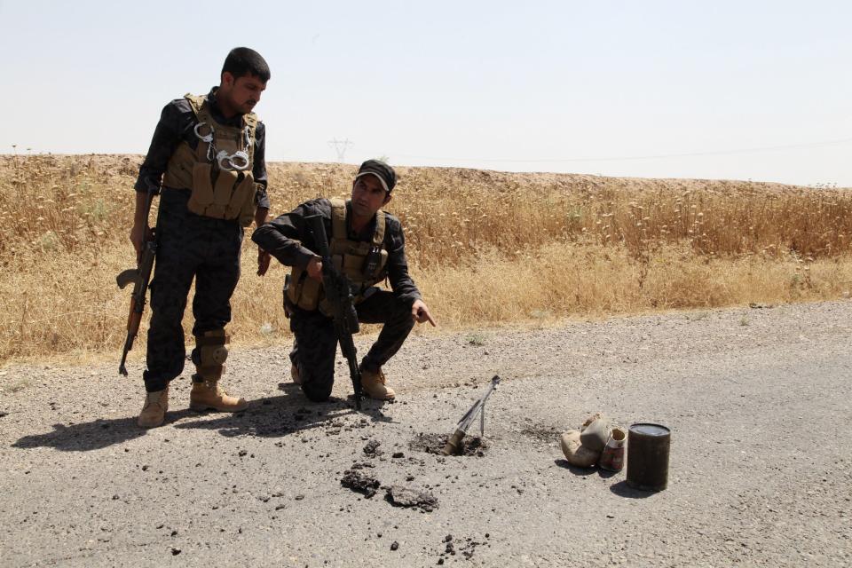 Members of the Kurdish security forces look at a mortar shell on a road in the outskirts of Kirkuk June 14, 2014. An offensive by insurgents that threatens to dismember Iraq seemed to slow on Saturday after days of lightning advances as government forces regained some territory in counter-attacks, easing pressure on the Shi'ite-led government in Baghdad. REUTERS/Azad Lashkari (IRAQ - Tags: CIVIL UNREST POLITICS MILITARY)