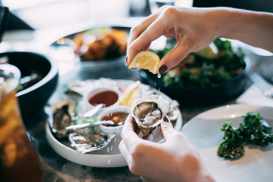 A woman's hand squeezing lemon juice on to a fresh oyster.