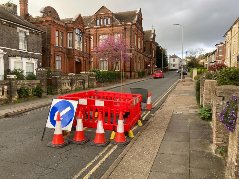 A sinkhole surrounding by barriers with Ipswich Museum in the background