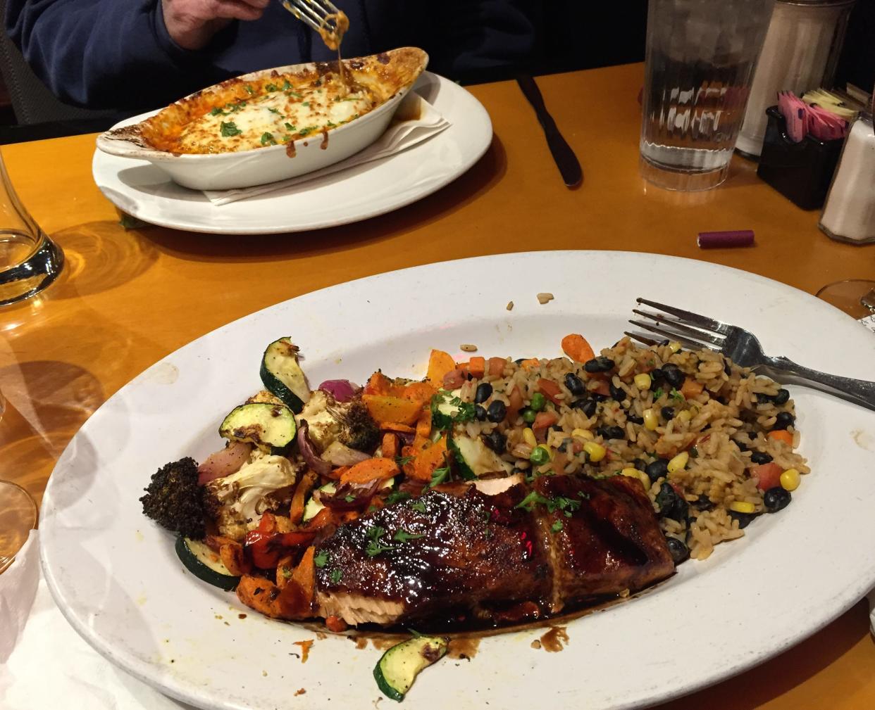 Pictured are One World Cafe's balsamic citrus salmon with black bean rice and vegetables, foreground, and eggplant lasagna, background.