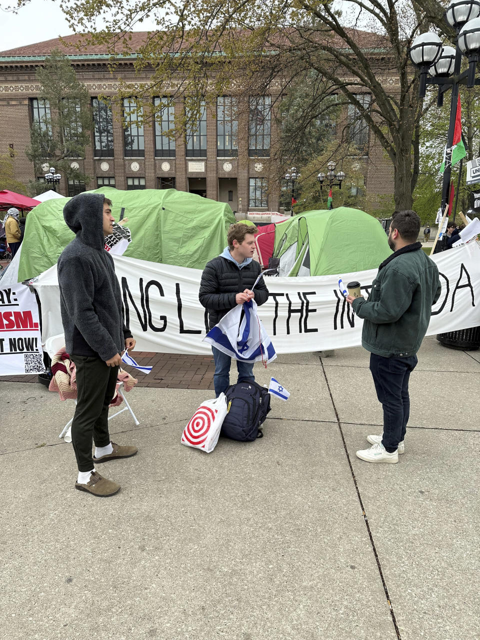 University of Michigan computer science junior Josh Brown, center, hands out miniature blue and white flags of Israel while standing Wednesday, April 24, 2024, in front of a banner reading “LONG LIVE THE INTIFADA" in Ann Arbor, Mich. The banner is part of a protest by students and groups demanding the Ann Arbor school divest from companies that do business with Israel. (AP Photo/Corey Williams)