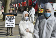 A religious street preacher stands alongside protesters who are calling for greater action from the government to prevent the spread of coronavirus, outside Downing Street in London, Monday March 16, 2020. For most people, the new coronavirus causes only mild or moderate symptoms, such as fever and cough. For some, especially older adults and people with existing health problems, it can cause more severe illness, including pneumonia. (Dominic Lipinski/PA via AP)