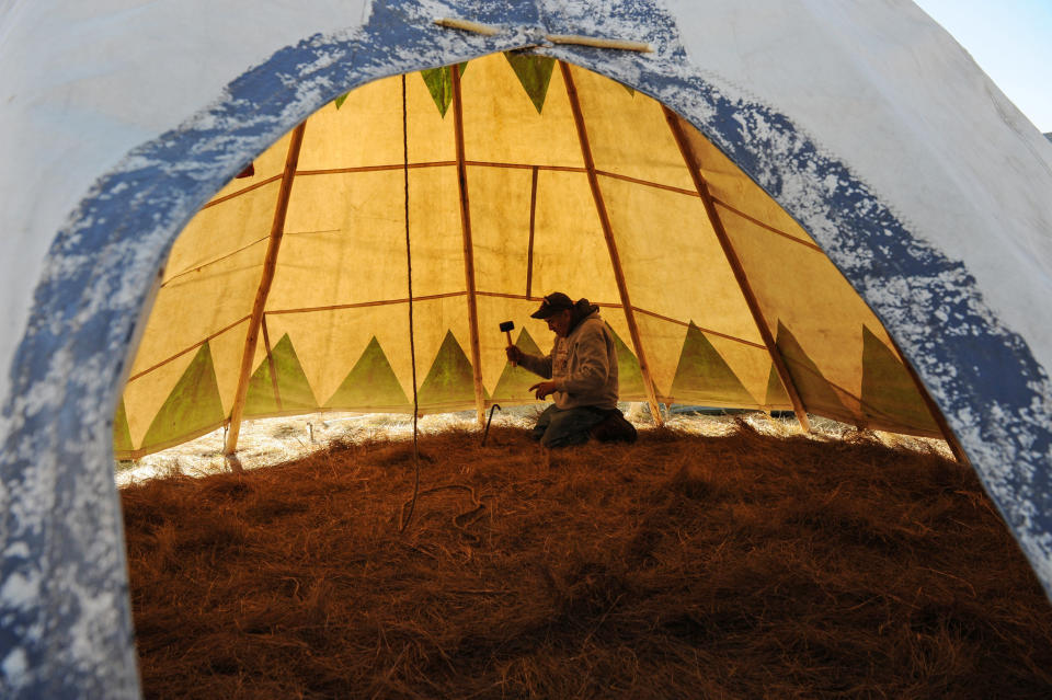 Steve Tamayo drives in stakes to his tipi in an encampment.