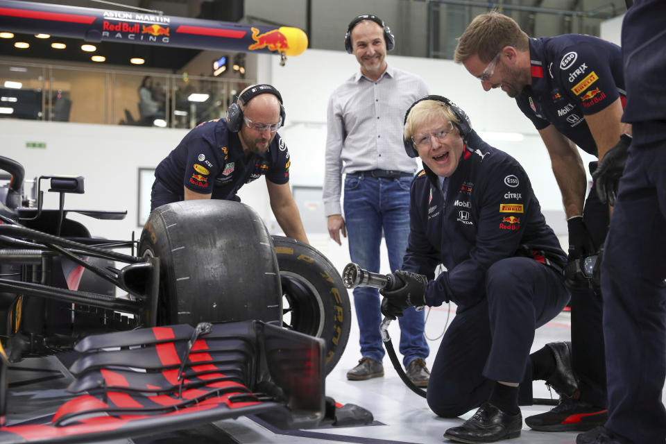 Boris Johnson is guided as he changes a wheel on a Formula One F1 car during a visit to Red Bull Racing facility in Milton Keynes