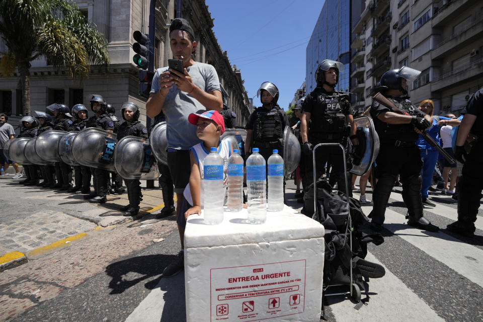 A demonstrator sells water on the sidelines of a protest outside Congress, where police stand guard, during a national strike against the economic and labor reforms proposed by Argentine President Javier Milei's government in Buenos Aires, Argentina, Wednesday, Jan. 24, 2024. (AP Photo/Natacha Pisarenko)