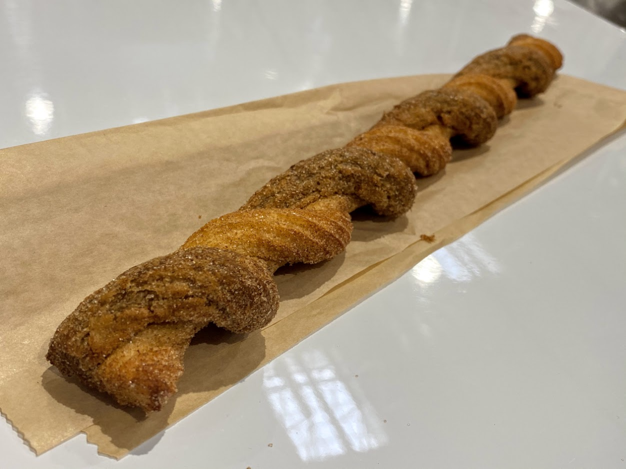 A churro at the Costco food court, on a brown serving bag, on a white table