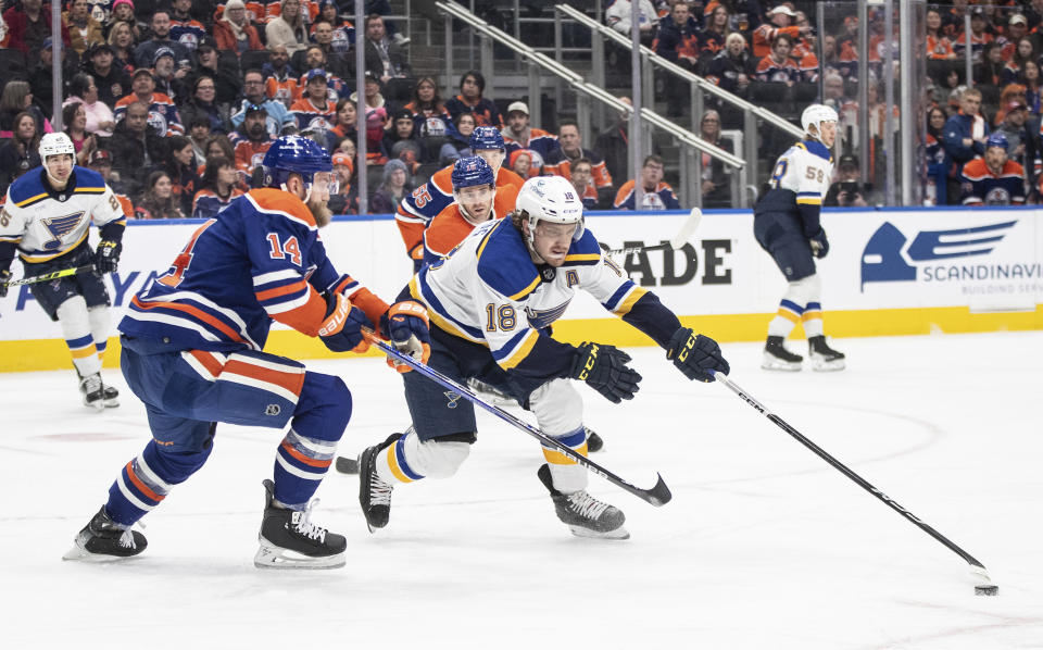 St. Louis Blues' Robert Thomas (18) reaches for the puck as Edmonton Oilers' Mattias Ekholm (14) defends during the first period of an NHL hockey game Wednesday, Feb. 28, 2024, in Edmonton, Alberta. (Jason Branson/The Canadian Press via AP)