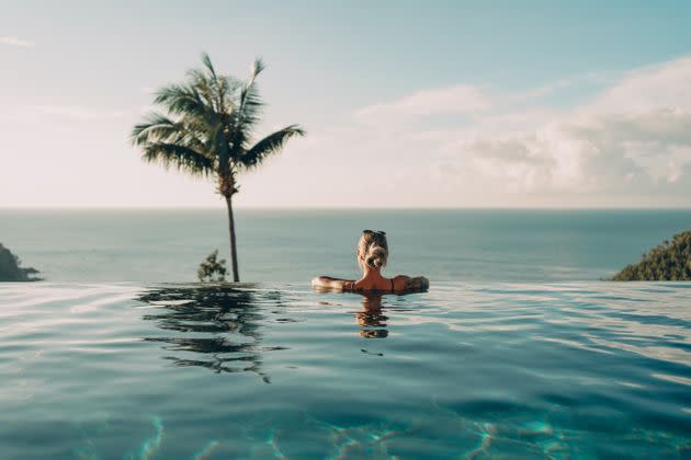 Rear view of a woman standing leaned at the edge of a pool and enjoying the amazing sea view. (Photo: Johnce via Getty Images)